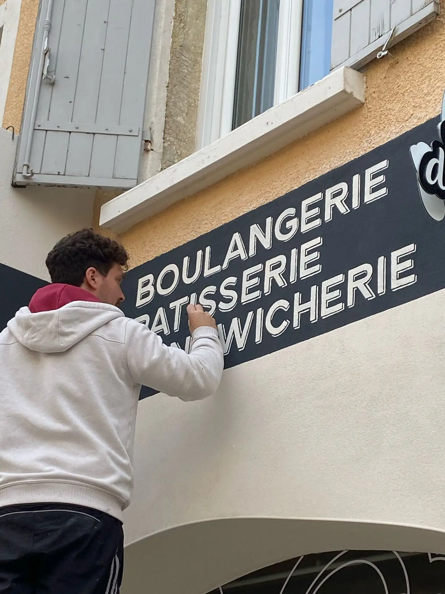 Flo en train de peindre le lettrage pour écrire &#34;boulangerie, patisserie, sandwicherie&#34;